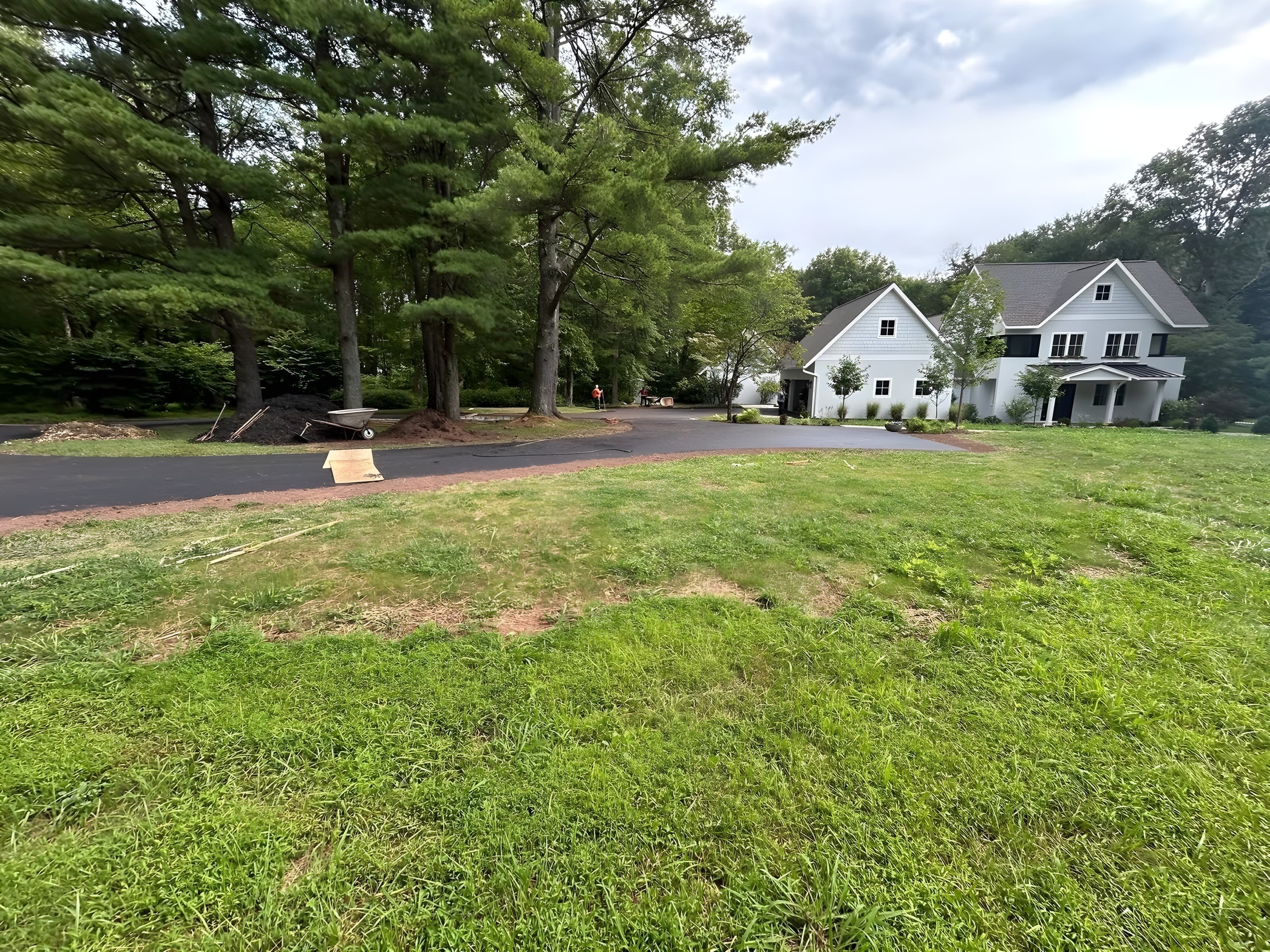 New black asphalt driveway curving past a white modern farmhouse with fresh topsoil edges