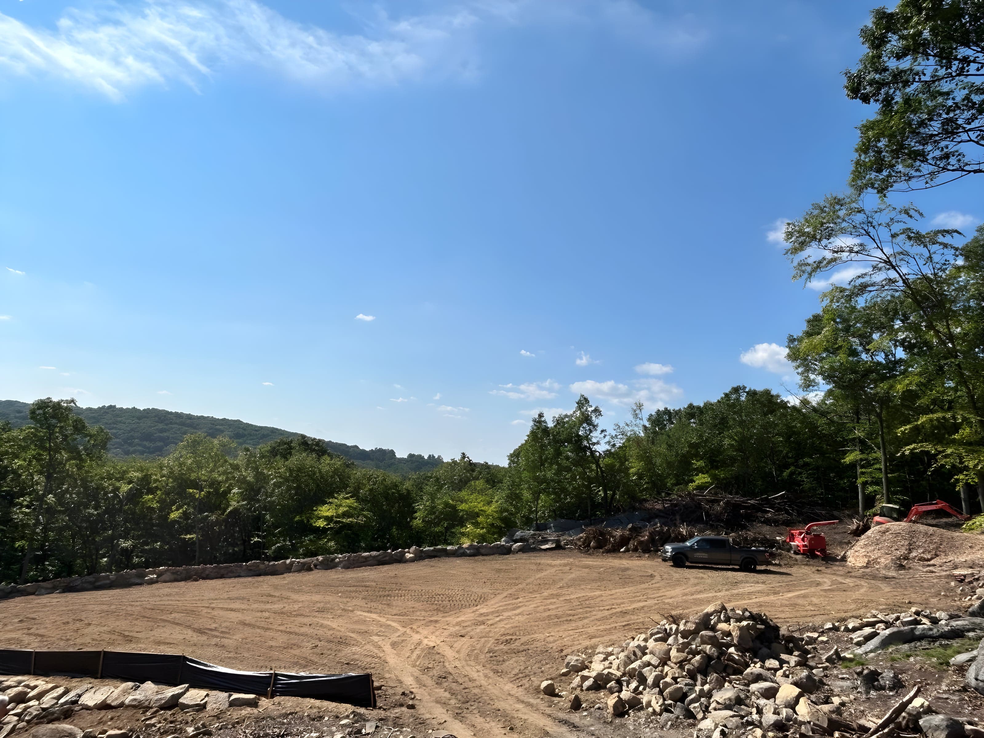 Wide graded hilltop pad ringed by stone with equipment at the tree line and ridgeline views