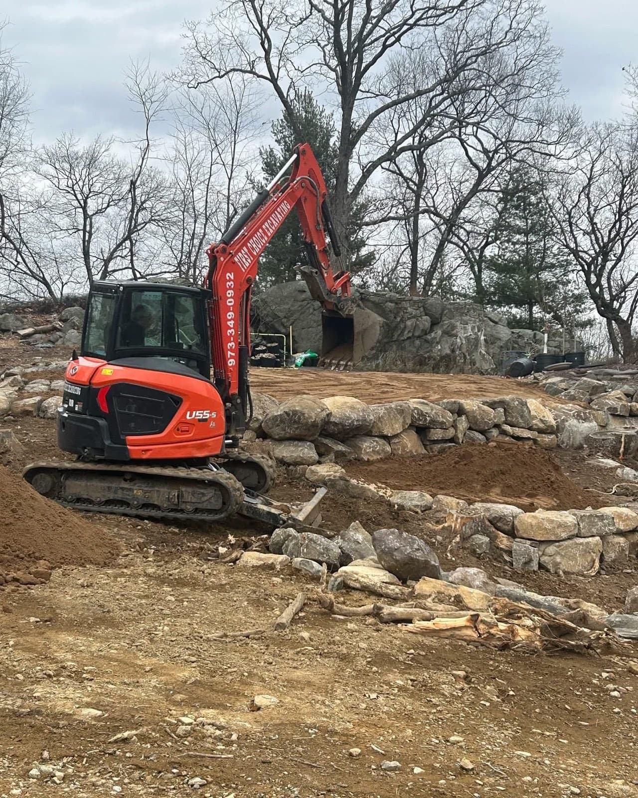 Excavator placing terraced boulder retaining walls on a rocky hillside